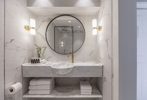 A bathroom with a marble sink, a round mirror, and two wall-mounted light fixtures.