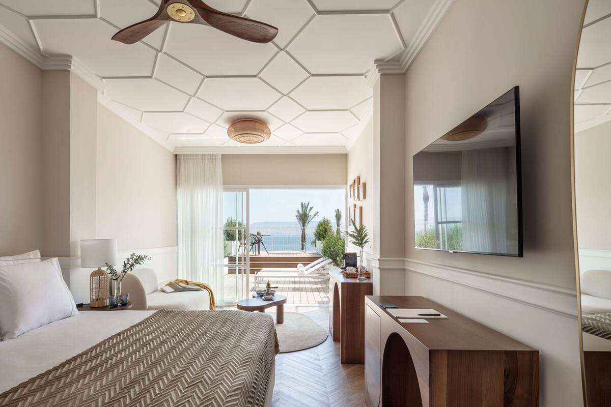 A hotel room with a large bed, a desk, a TV, and a balcony with a view.