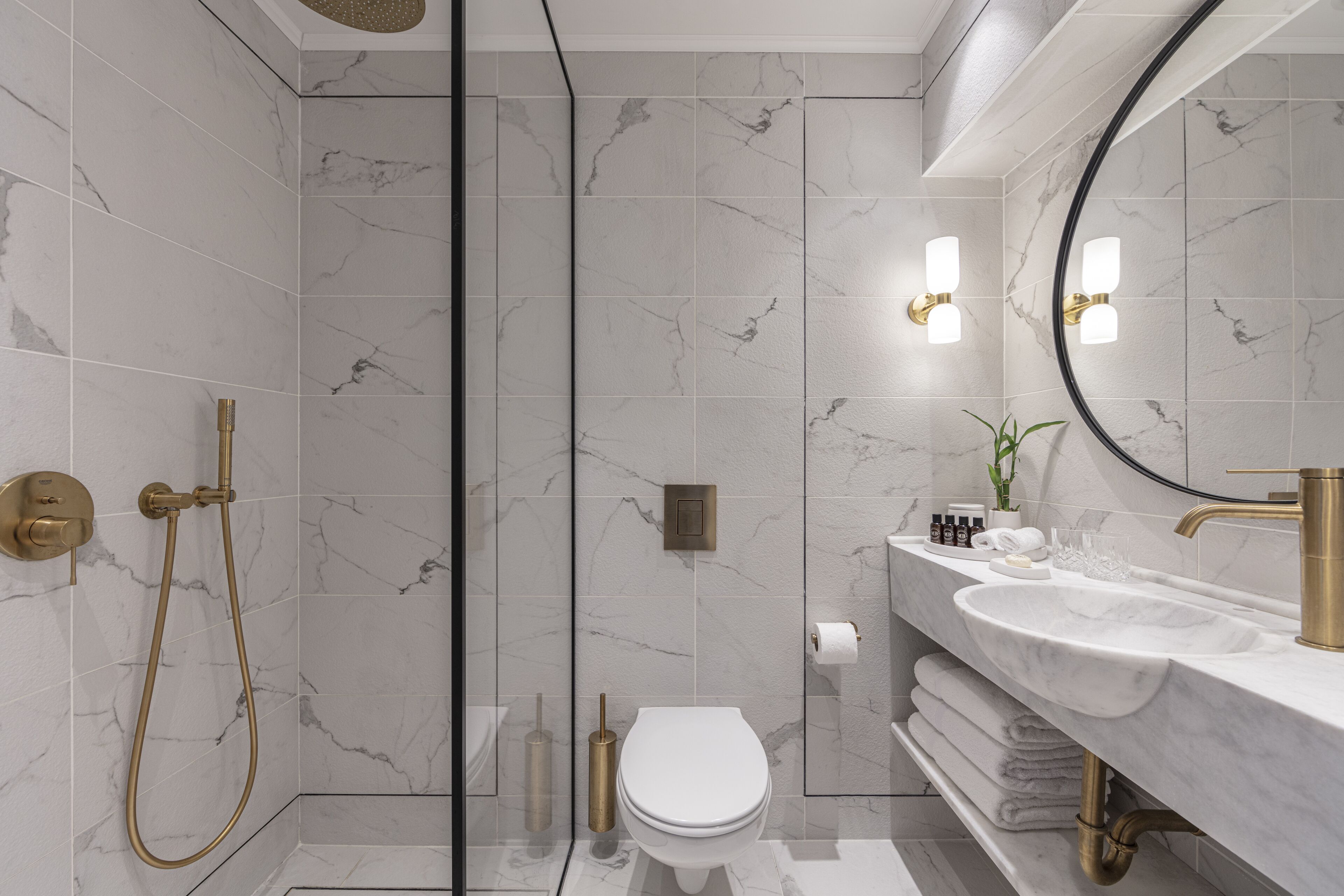 A modern bathroom with a glass-enclosed shower, a white toilet, and a marble-tiled vanity with a gold faucet.