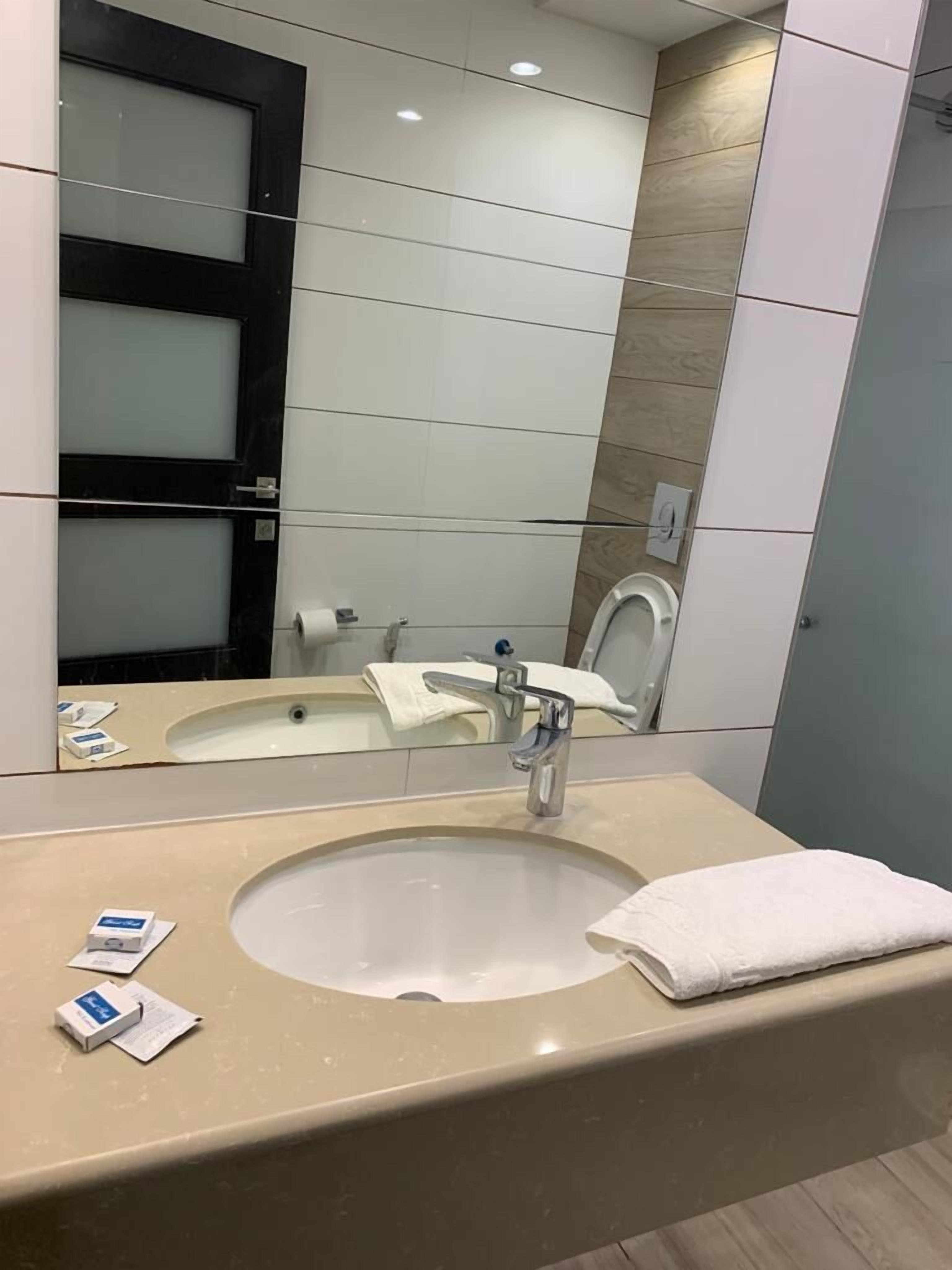 A modern bathroom with a large mirror, a sink, and a toilet.