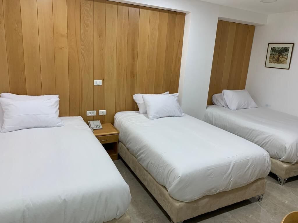 Hotelkamer met drie enkele bedden, houten lambrisering aan de wanden, een nachtkastje met telefoon en een klein schilderij.