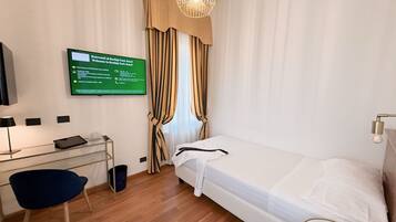 Quarto de hotel com uma cama, uma escrivaninha com computador, uma cadeira, televisão e um sinal com informações do hotel.