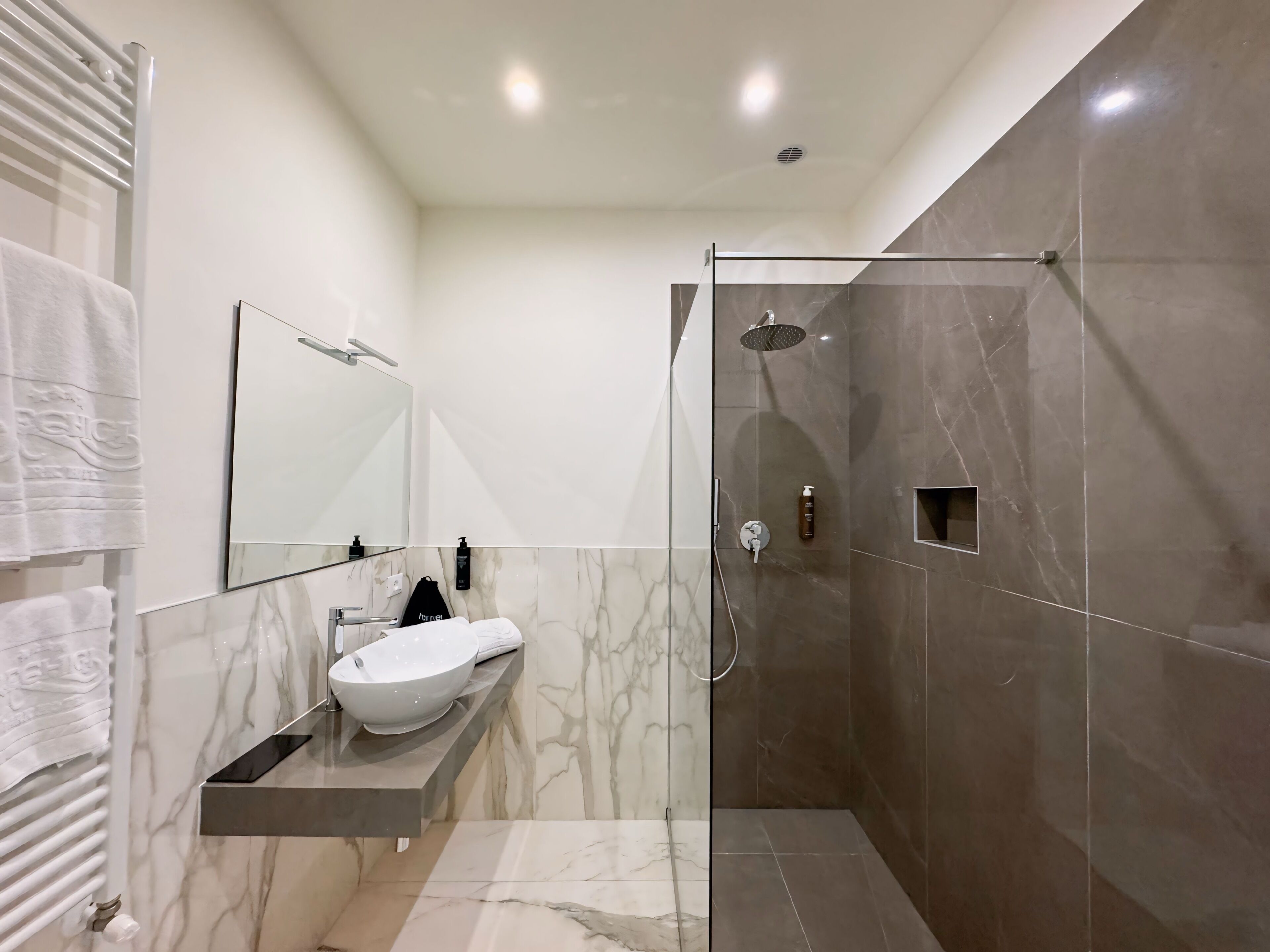 Un baño moderno con ducha de vidrio, lavamanos de mármol y un perchero para toallas.
