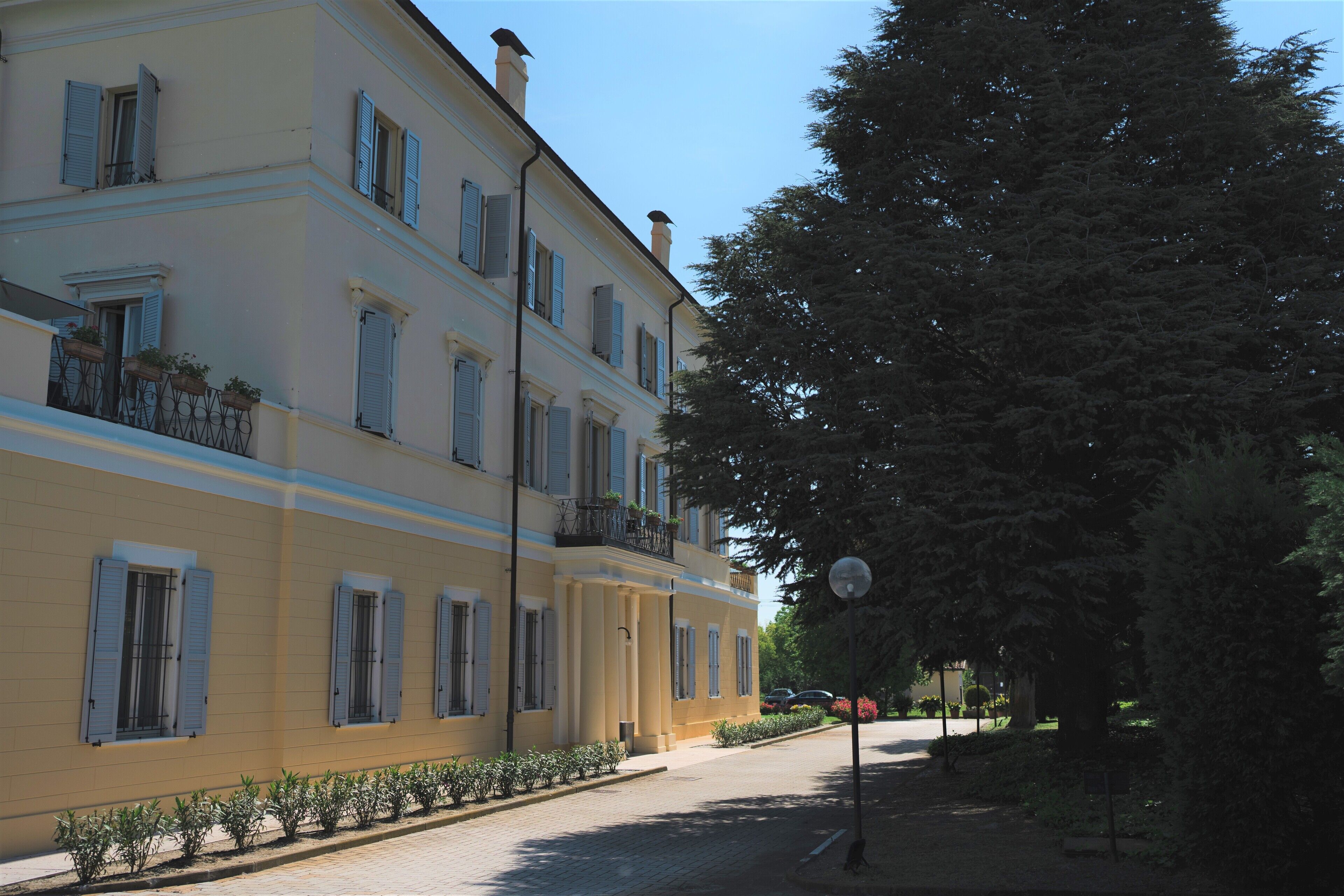 A multi-story building with balconies, a paved street, and trees.