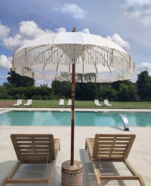 A poolside area with two wooden lounge chairs, a white umbrella, and a clear view of the pool. - Rechigi Park Hotel (Modena)