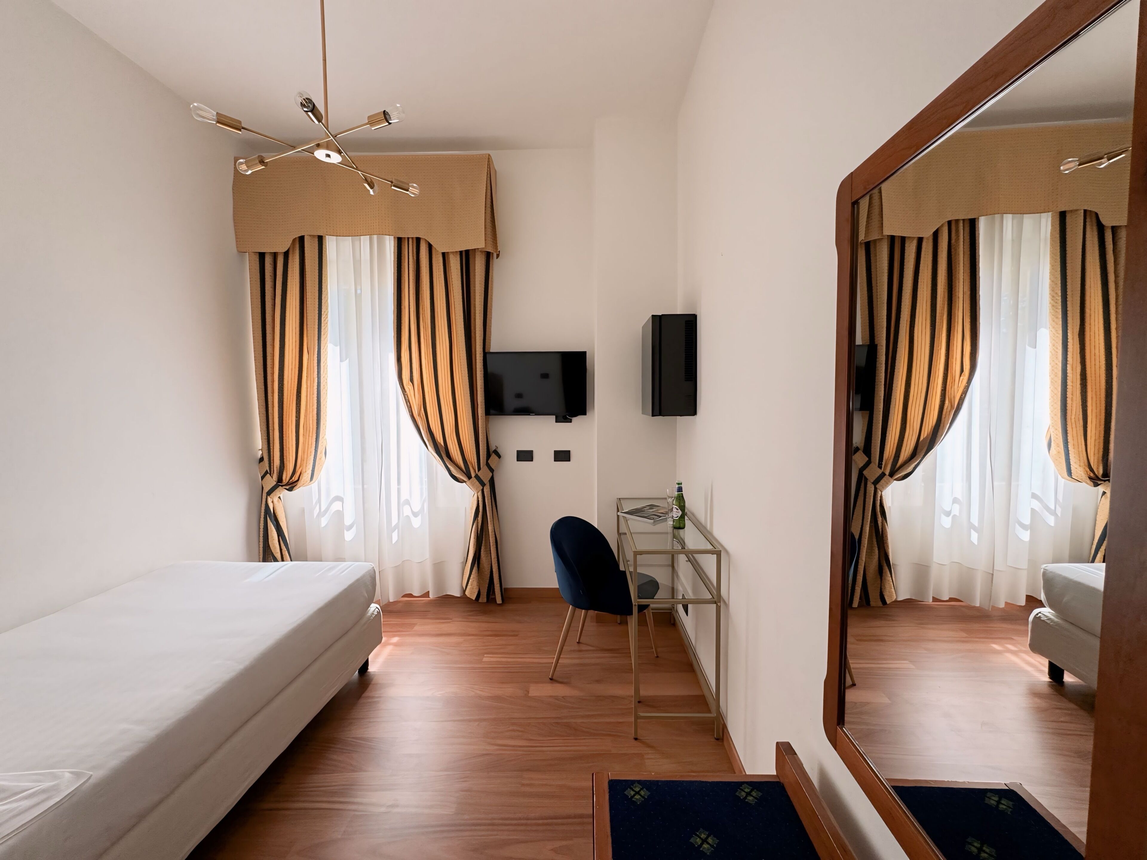 Una habitación de hotel con cama, escritorio, silla, televisor y cortinas.