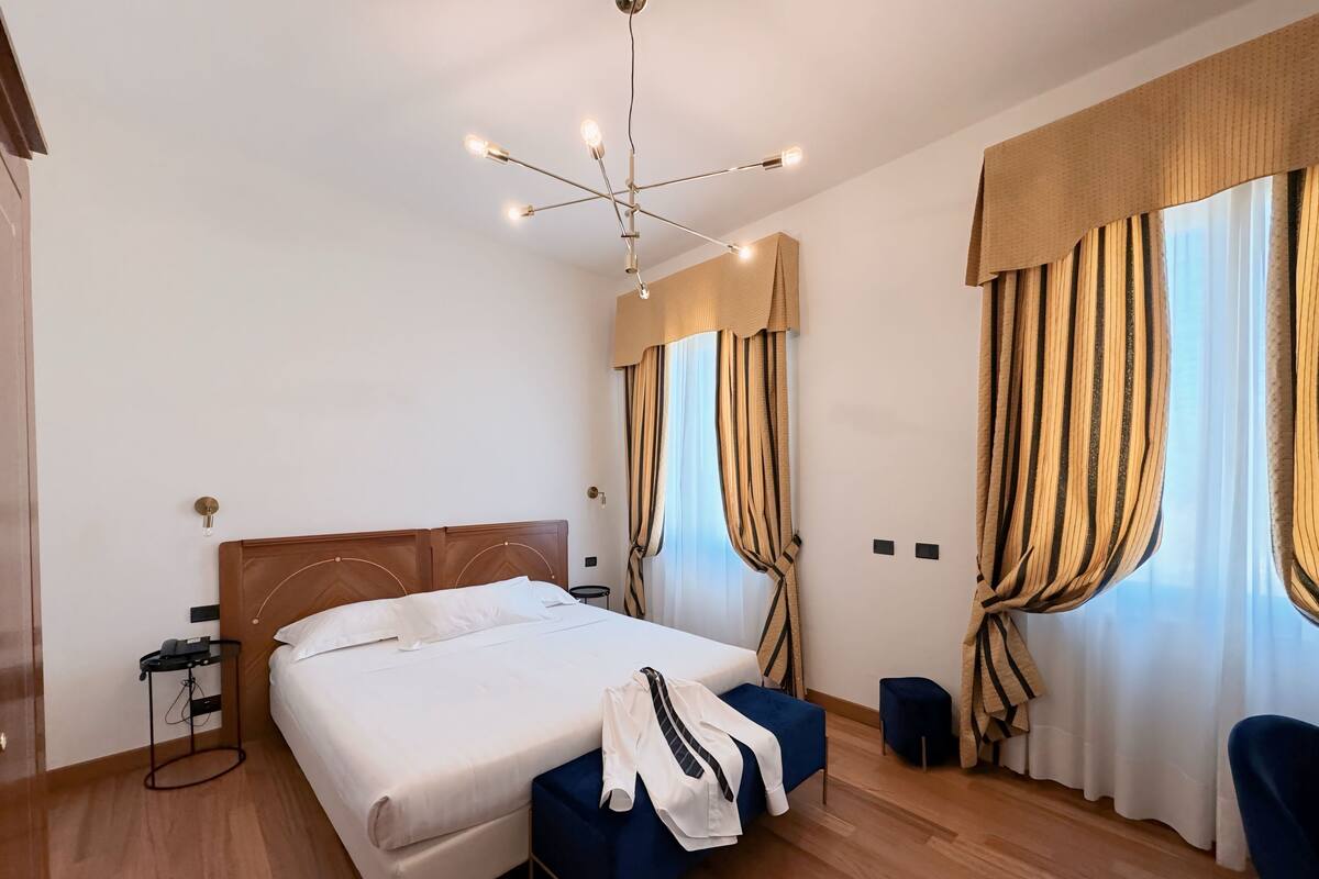 A hotel room with a large bed, a bedside table, a chair, and a ceiling light fixture.