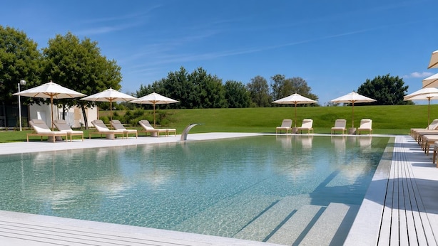 A swimming pool with lounge chairs and umbrellas, surrounded by a wooden deck and greenery. - Rechigi Park Hotel (Modena)
