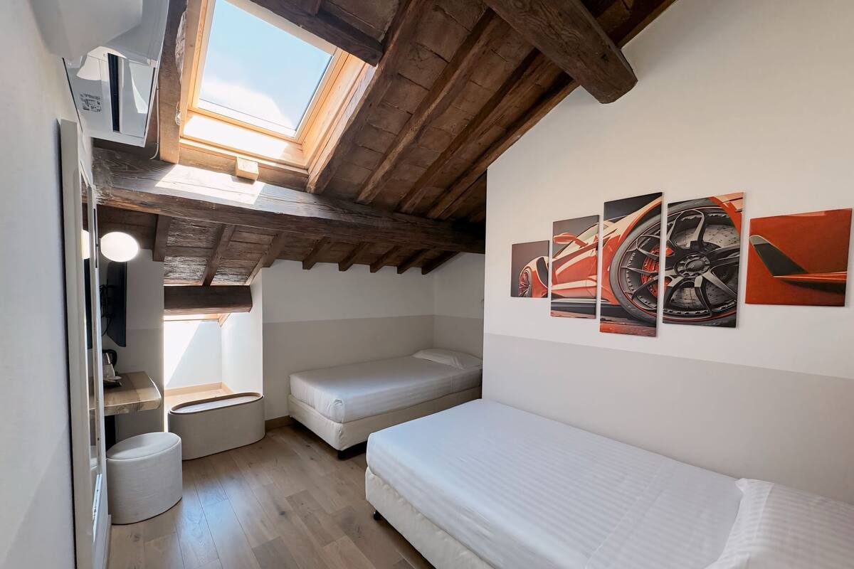 A compact room with a sloped ceiling, a skylight, a bed, a small table, and a wall-mounted artwork.