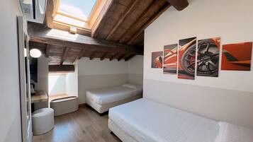 Ein kompakter Raum mit schrägem Dach, einem Oberlicht, einem Bett, einem kleinen Tisch und einem an der Wand hängenden Kunstwerk.