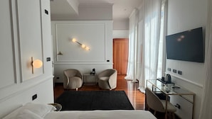 A modern hotel room with a large bed, a desk with a chair, a television, and a seating area with chairs. - Rechigi Park Hotel (Modena)