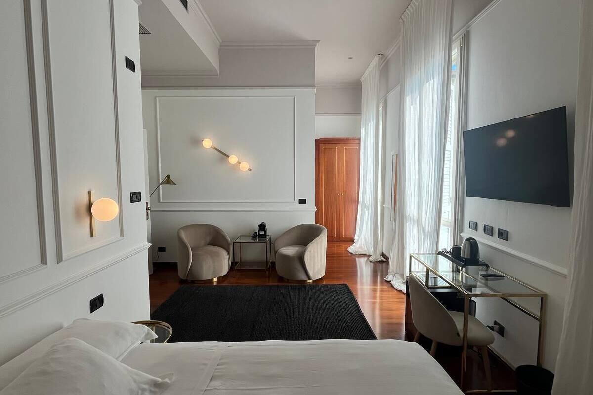 A modern hotel room with a large bed, a desk with a chair, a television, and a seating area with chairs.