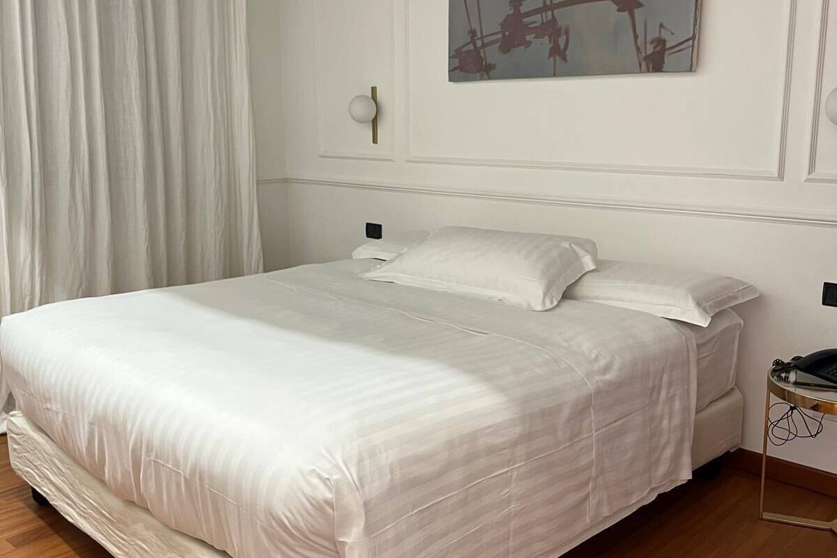 A neatly made bed in a room with a wooden floor, a white wall, and a painting above it.