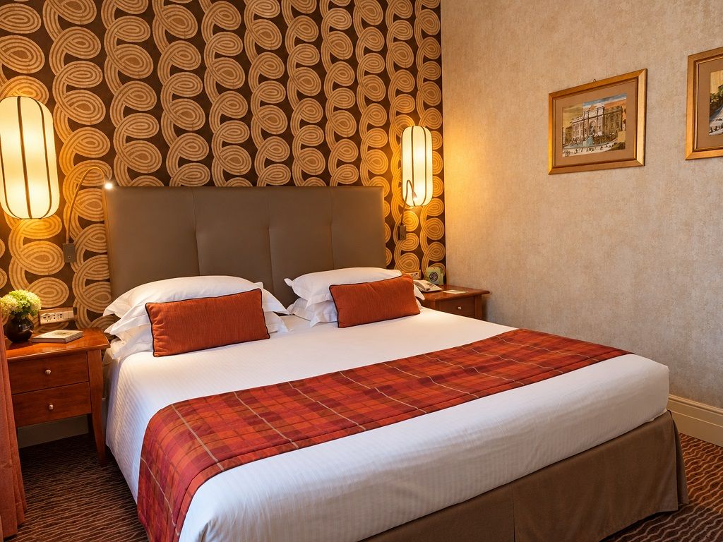 A hotel room with a large bed, two bedside tables, a headboard, and a patterned wallpaper.