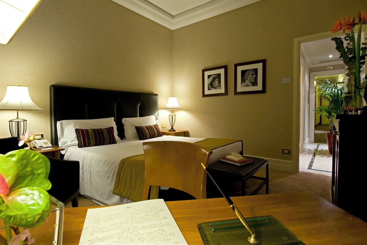 A hotel room with a bed, bedside tables, a desk with a chair, and a view of the hallway.