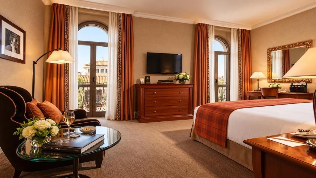 Una habitación de hotel con cama, escritorio, televisor, cómoda y vistas al balcón.