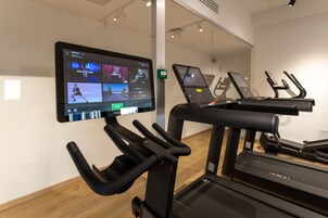 A gym with exercise equipment and a digital screen displaying workout videos.