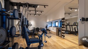 Ein Fitnessraum mit verschiedenen Trainingsgeräten, einer Spiegelwand und Holzboden.