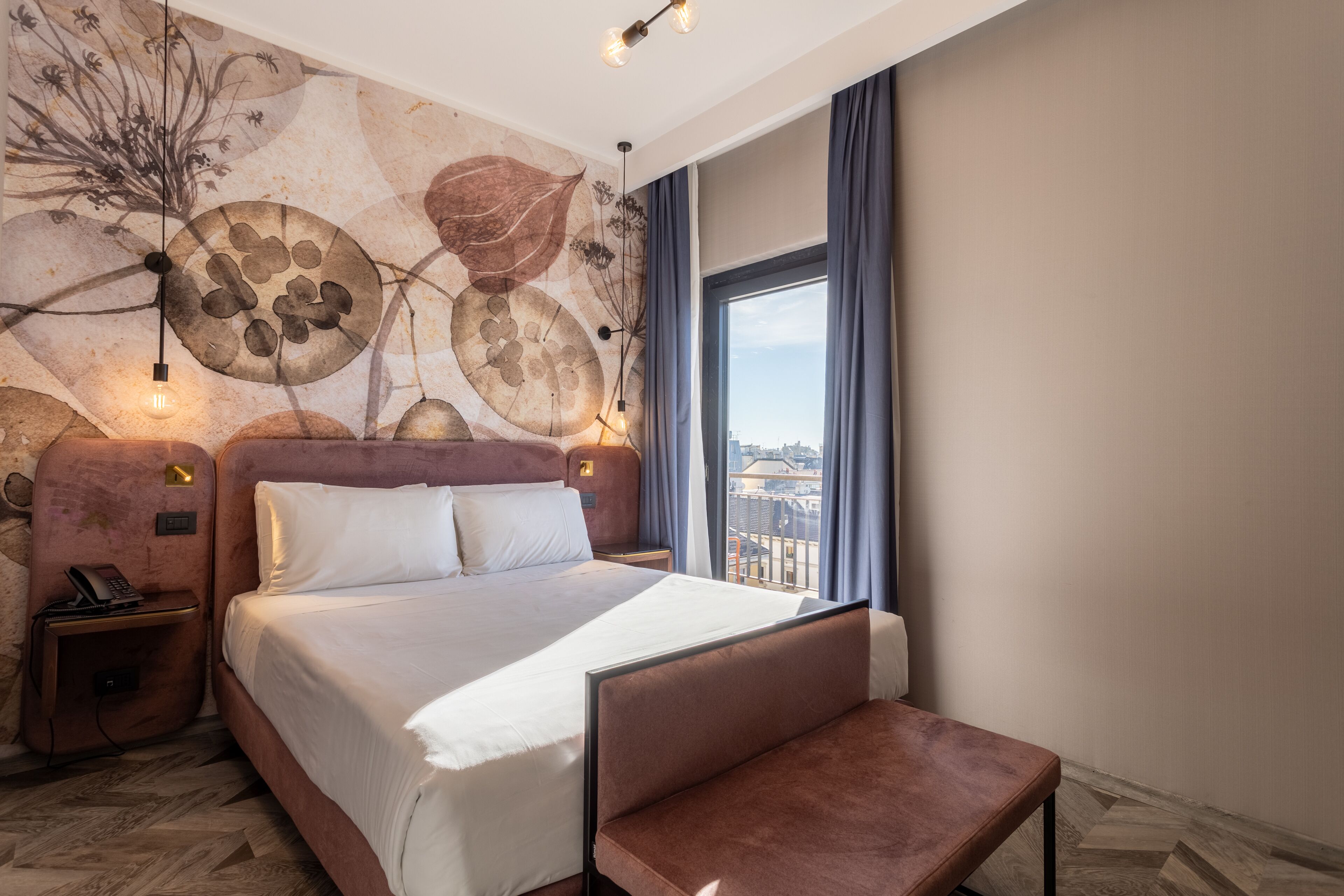 A hotel room with a large bed, a bench, a nightstand with a phone, and a wall mural.