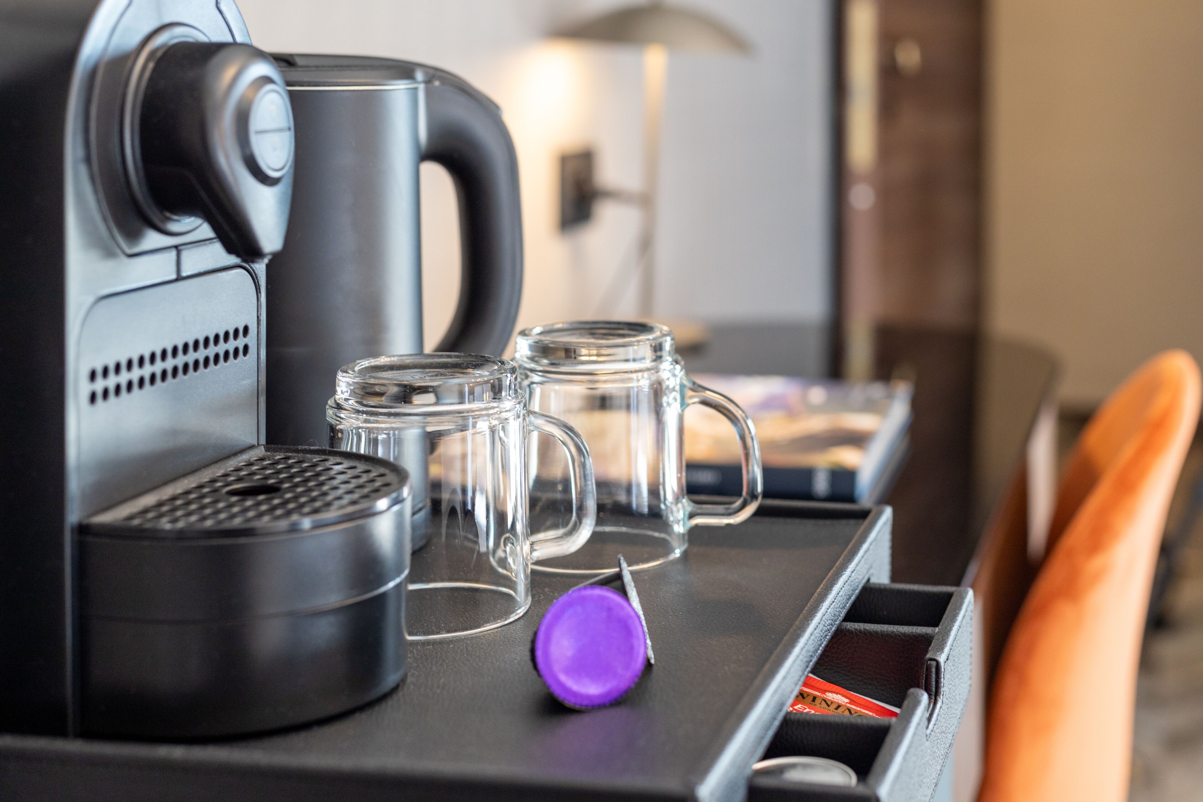 A coffee machine with a purple button, two clear mugs, and a kettle on a countertop.