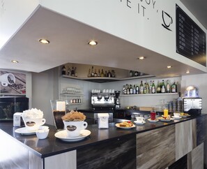 Een moderne bar met een koffiehoek, espresso machines en een divers assortiment drankflessen.