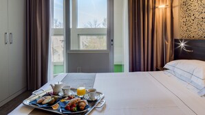 A hotel room with a bed, a breakfast tray with croissants, fruit, and beverages, a wardrobe, and a view of the outside. - Best Western Plus Hotel Farnese (Parma)