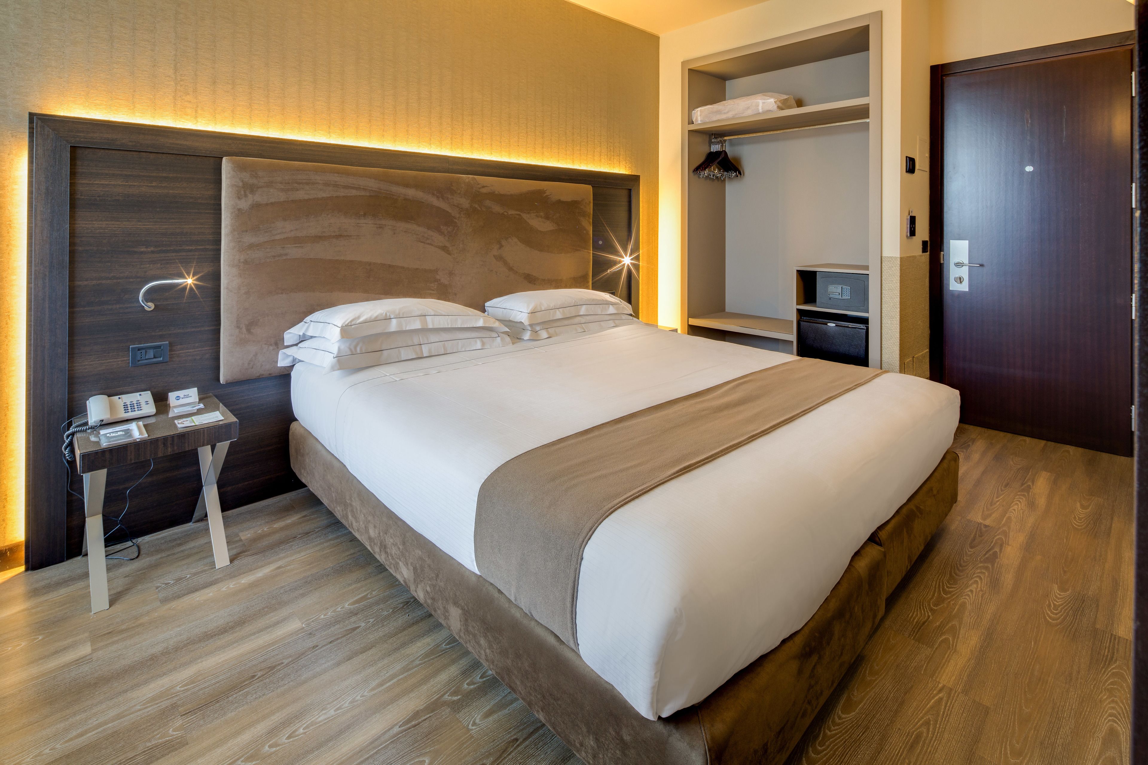 Et moderne hotelværelse med en stor seng, sengeborde, et garderobeskab og et skrivebord med telefon.