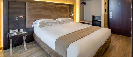 A modern hotel room with a large bed, bedside tables, a wardrobe, and a desk with a telephone.