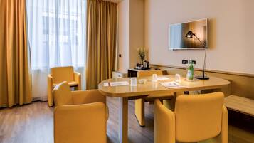 Ein Hotelzimmer mit einem runden Tisch, vier gelben Stühlen, einem flachbildfernseher an der Wand und Holzboden.