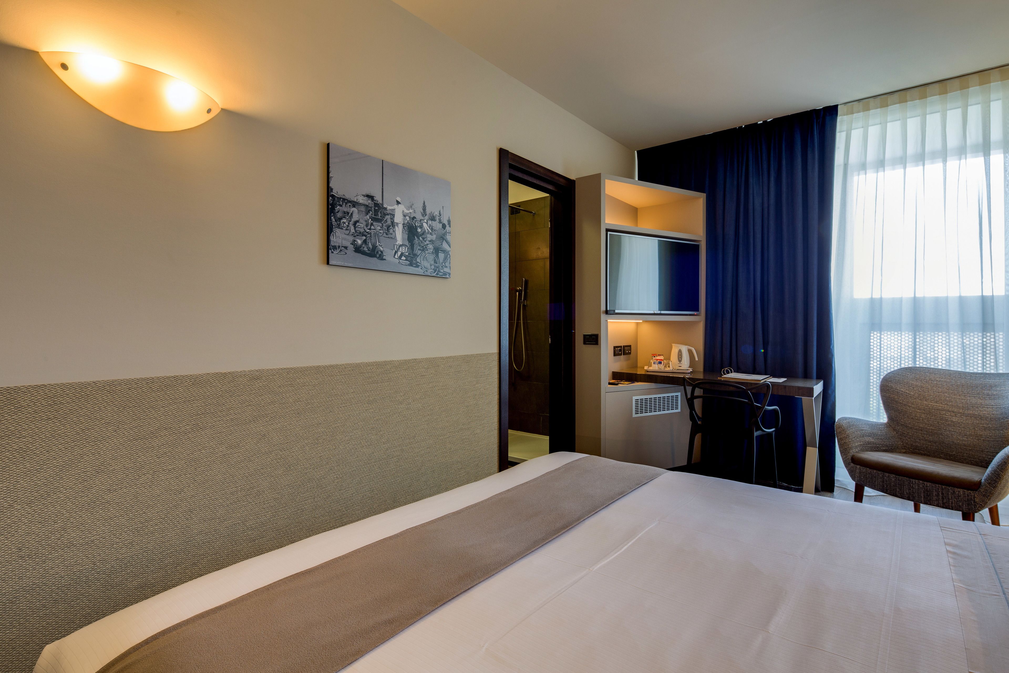 A hotel room with a bed, a desk with a chair, a television, and a shower area.