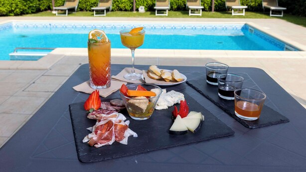 A poolside table with a variety of food and drinks, including a glass of iced tea, a cocktail, and several plates of appetizers. - Best Western Plus Hotel Farnese (Parma)