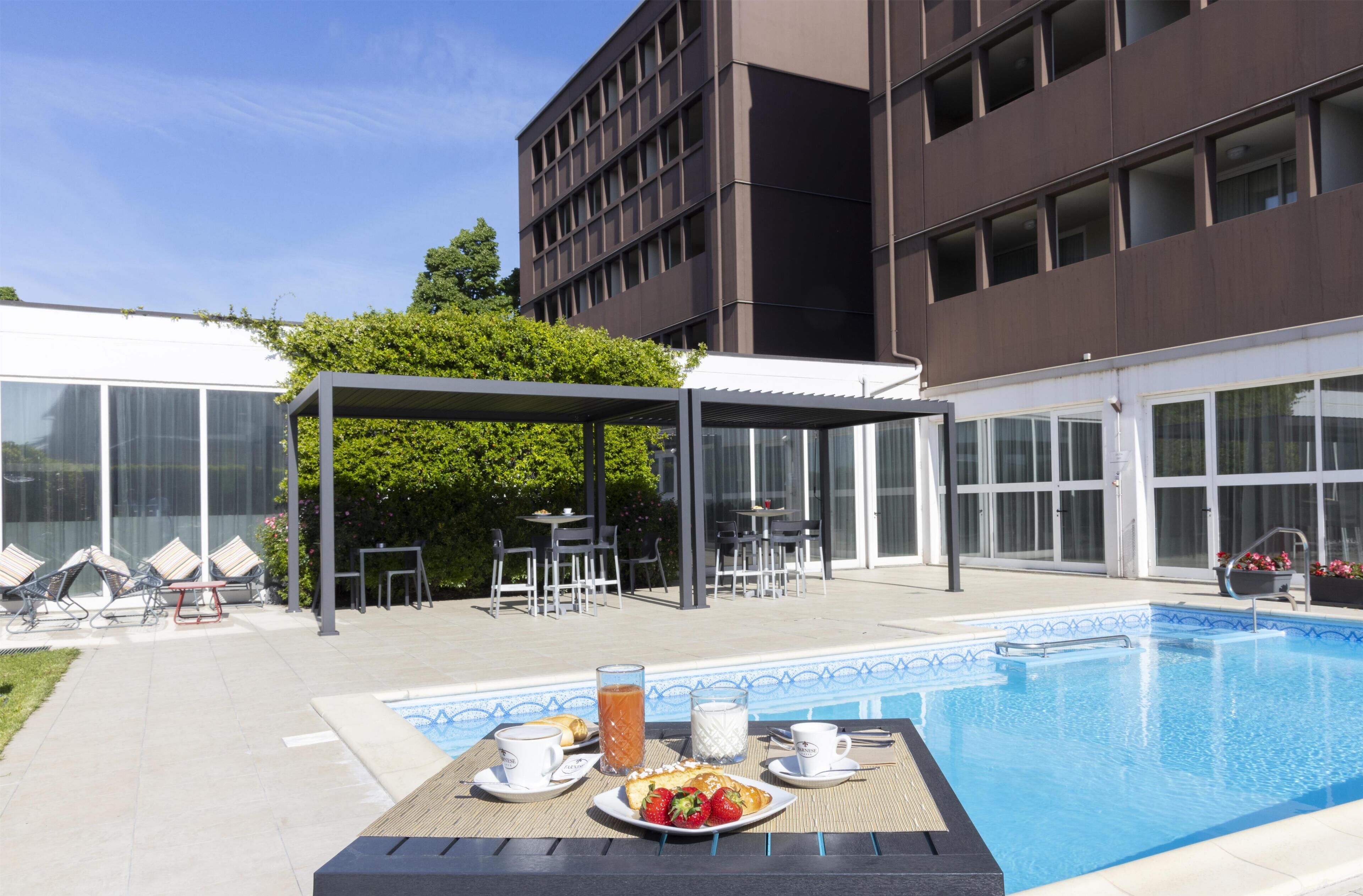 Un espace aménagé au bord de la piscine, avec une table dressée pour le petit-déjeuner, des sièges extérieurs et une terrasse couverte.