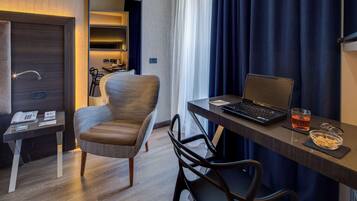 A hotel room with a desk, laptop, and a chair. There is a telephone on the desk and a bowl of snacks on the table.