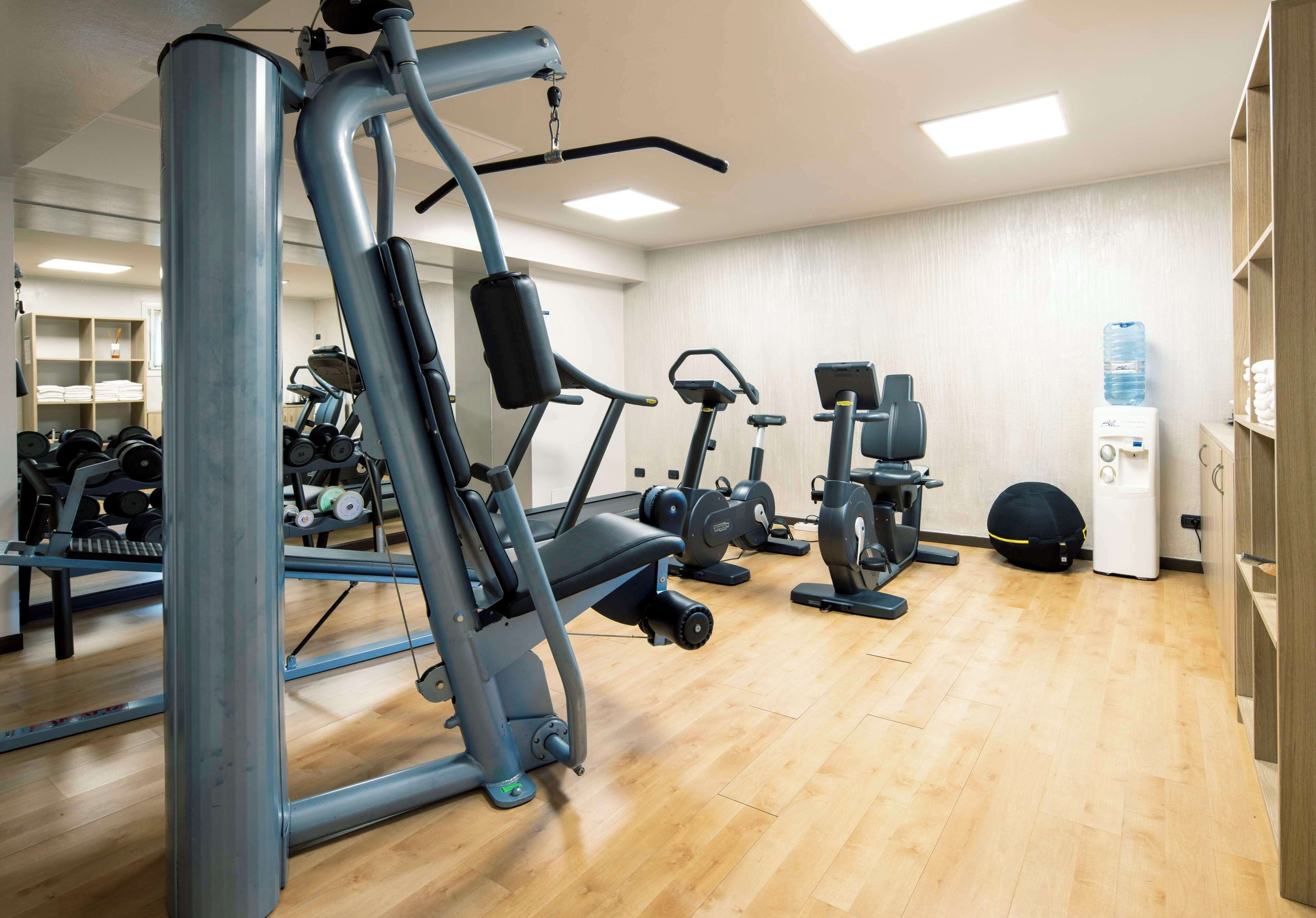 Ein Fitnessstudio mit verschiedenen Trainingsgeräten, einem Wasserspender und ordentlich angeordneten Gewichten.