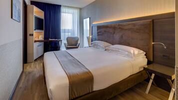 A hotel room with a large bed, a desk with a chair, a television, and a window with curtains.