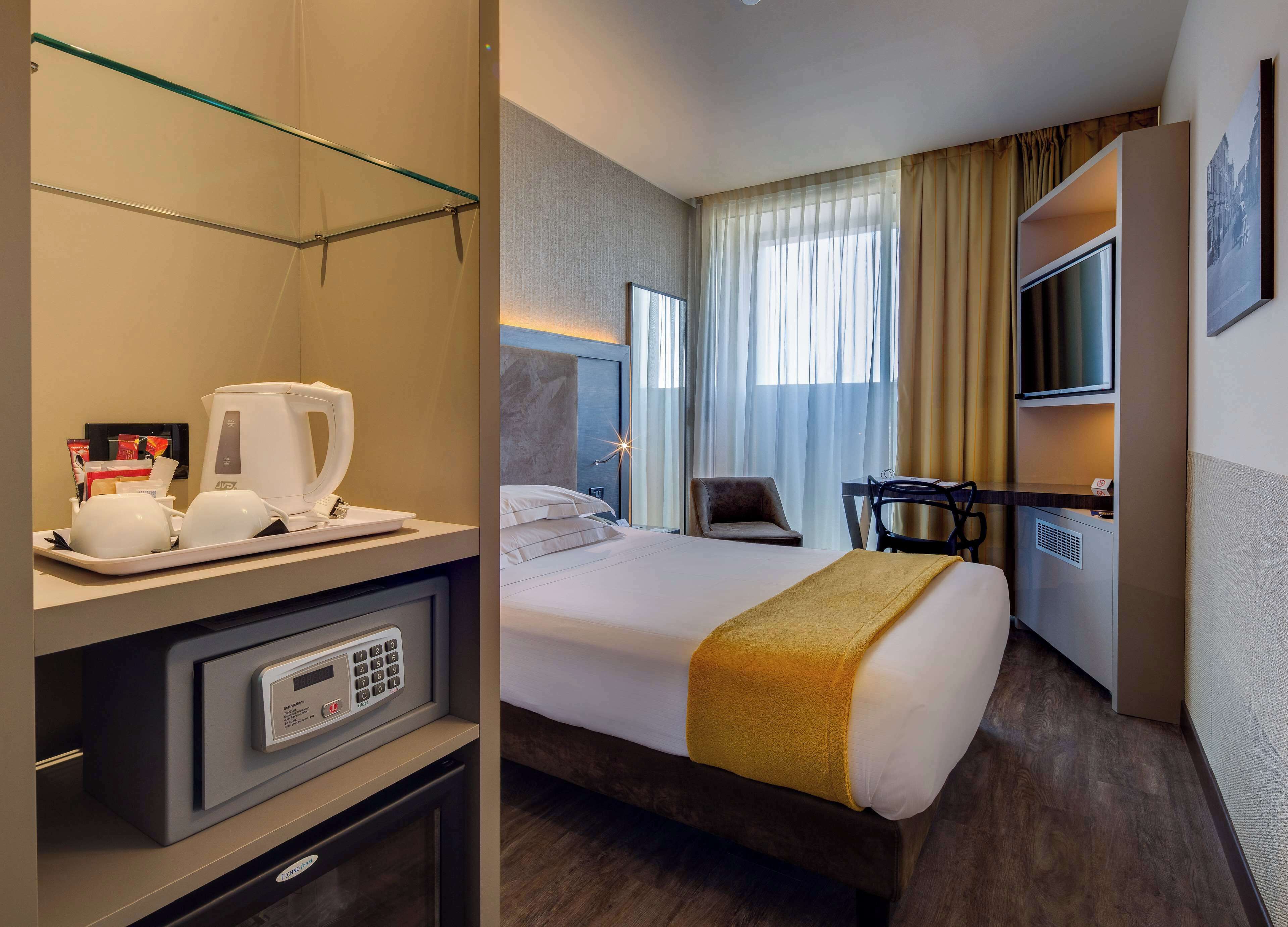Una camera d'albergo con un letto, una scrivania, una sedia, una televisione e un minibar.