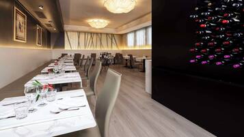 Un espace repas avec de longues tables dressées pour le repas, un meuble à vin sur le côté droit et des œuvres d’art encadrées accrochées aux murs.