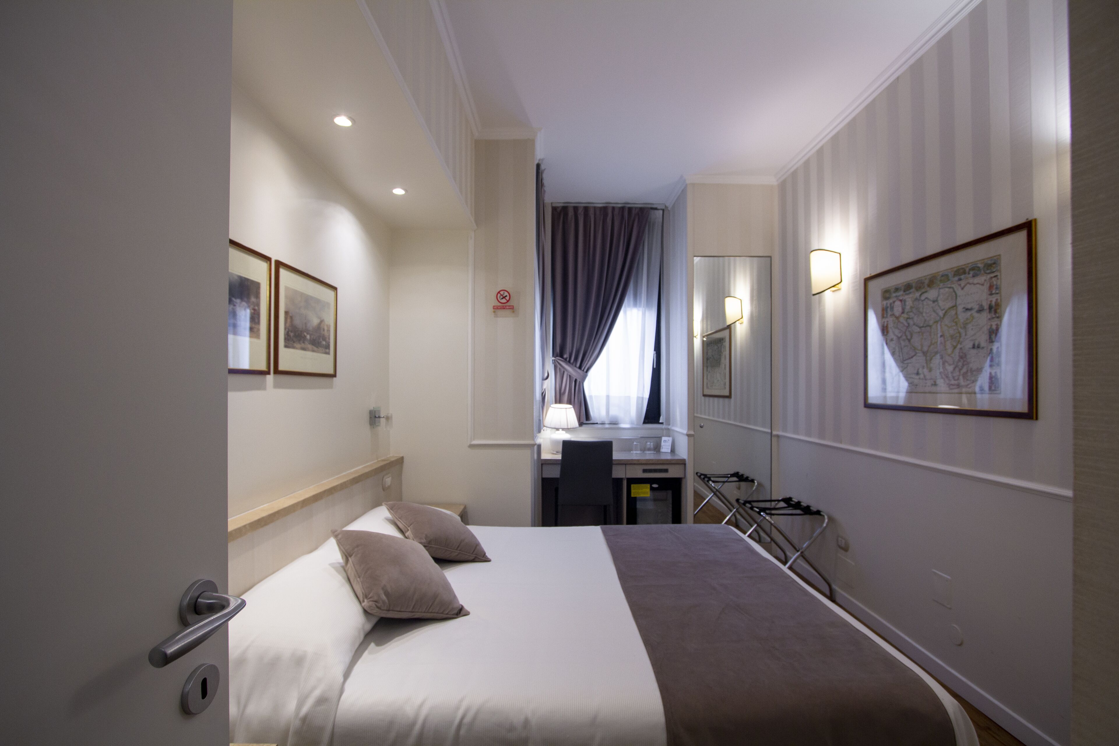 Une chambre d’hôtel avec un lit, un bureau, une chaise, une lampe, une carte accrochée au mur et une porte.