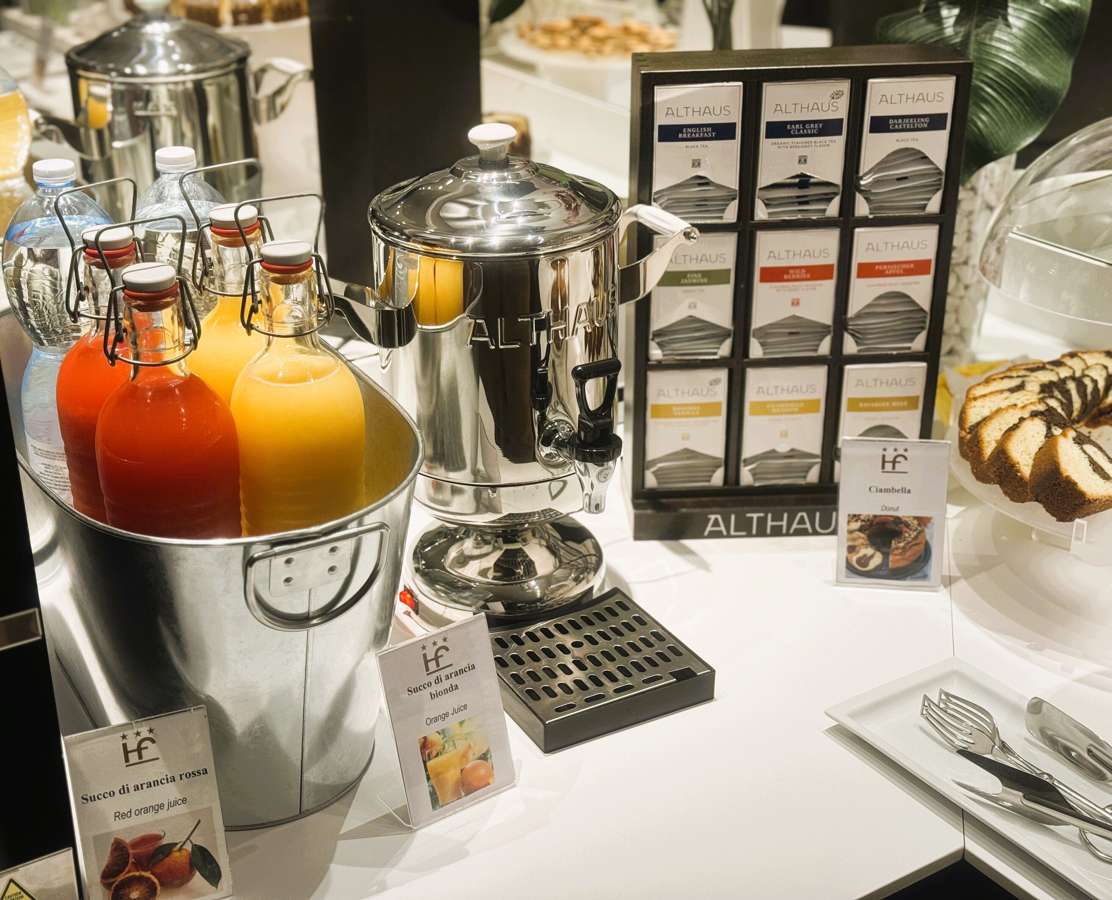 Zona de bufé con diversas opciones de comida y bebida, incluyendo una selección de jugos y una variedad de bolsitas de té.