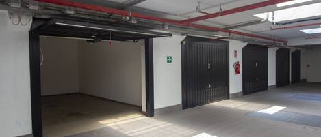 A clean, well-lit hallway with tiled floors, red and white pipes on the ceiling, and black doors.