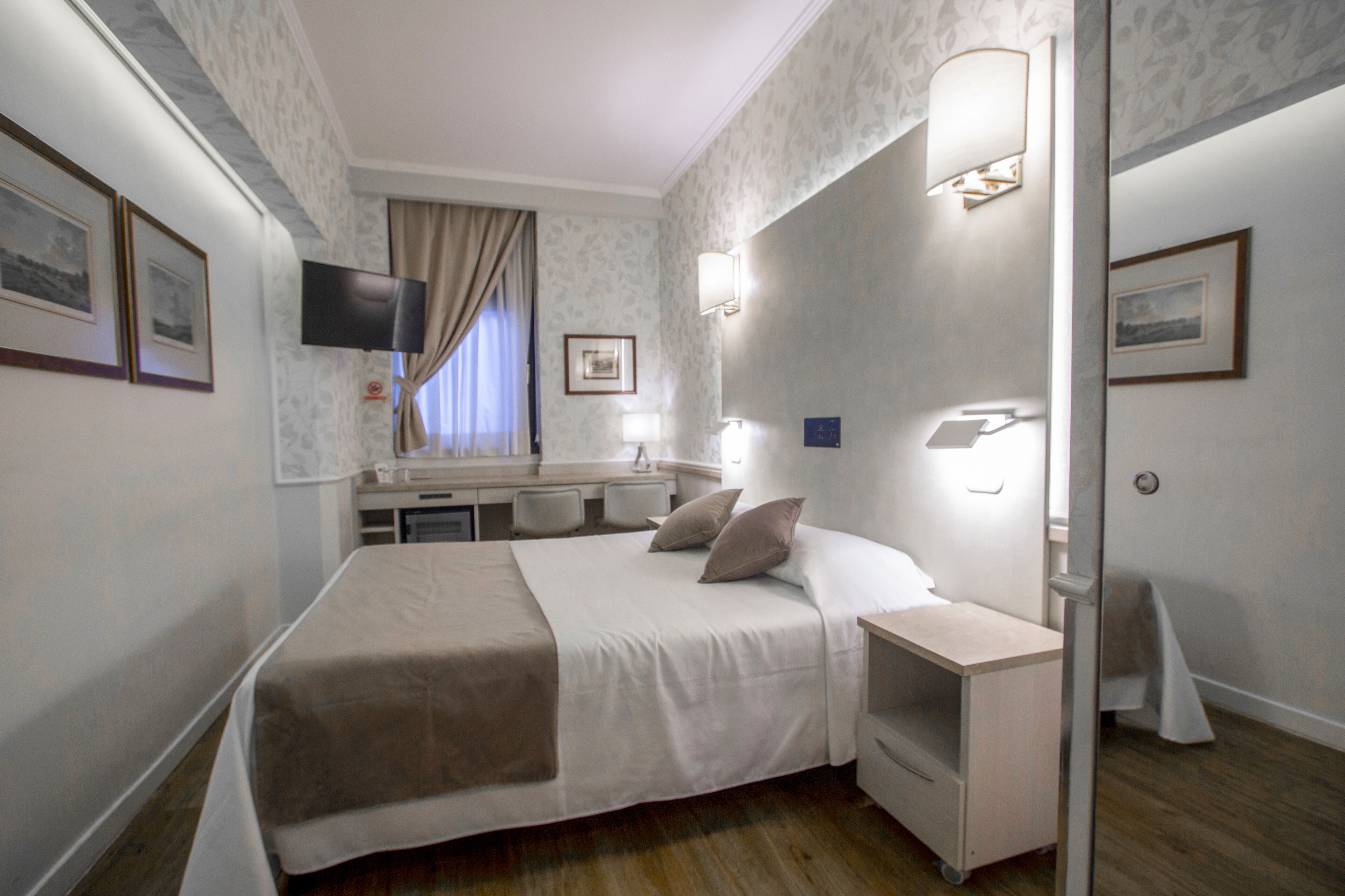 Una habitación de hotel con cama, mesita de noche, lámpara y escritorio con silla.