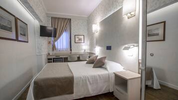 Ein Hotelzimmer mit Bett, Nachttisch, Lampe und Schreibtisch mit Stuhl.