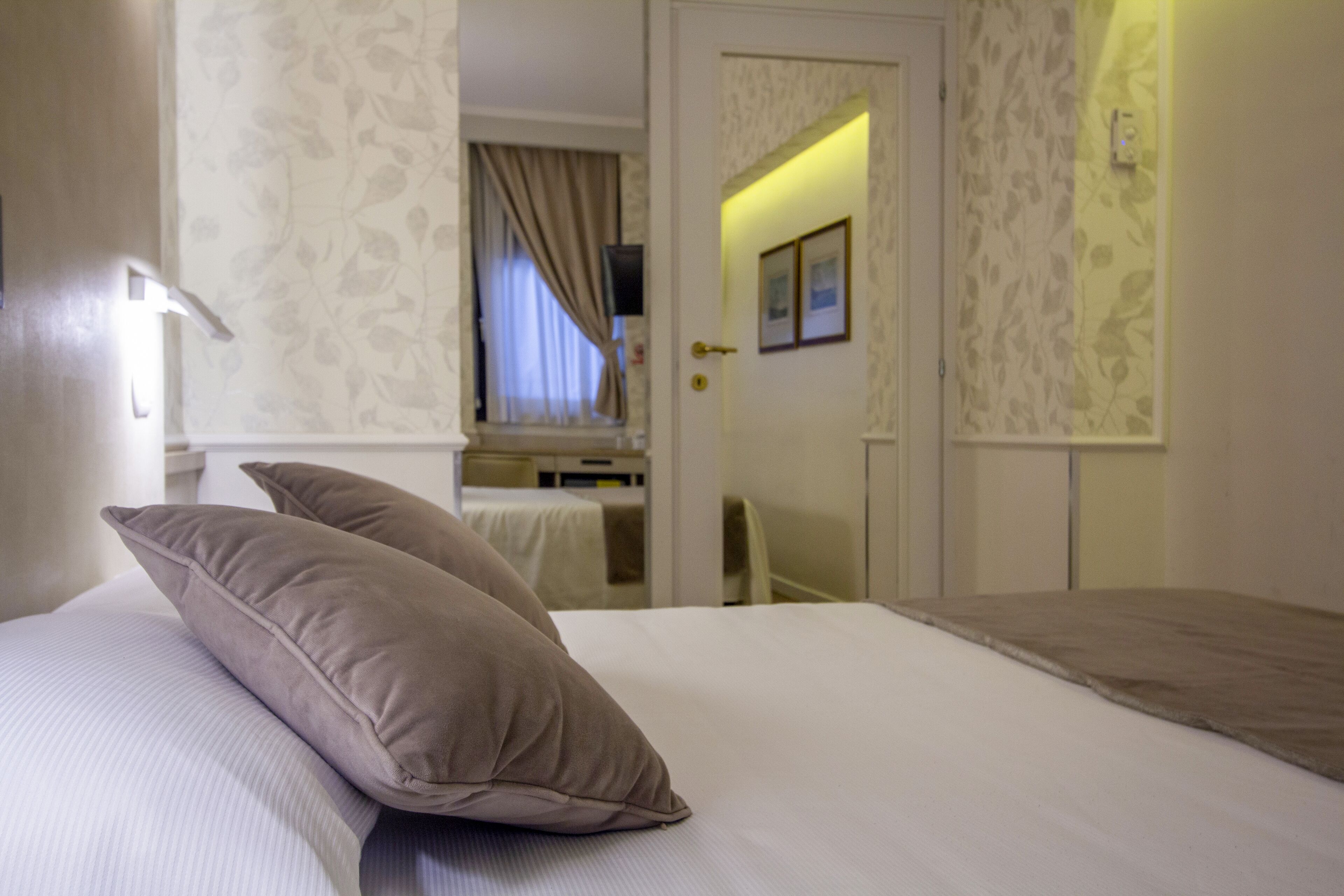 A hotel room with a bed, pillows, a desk, and a chair.