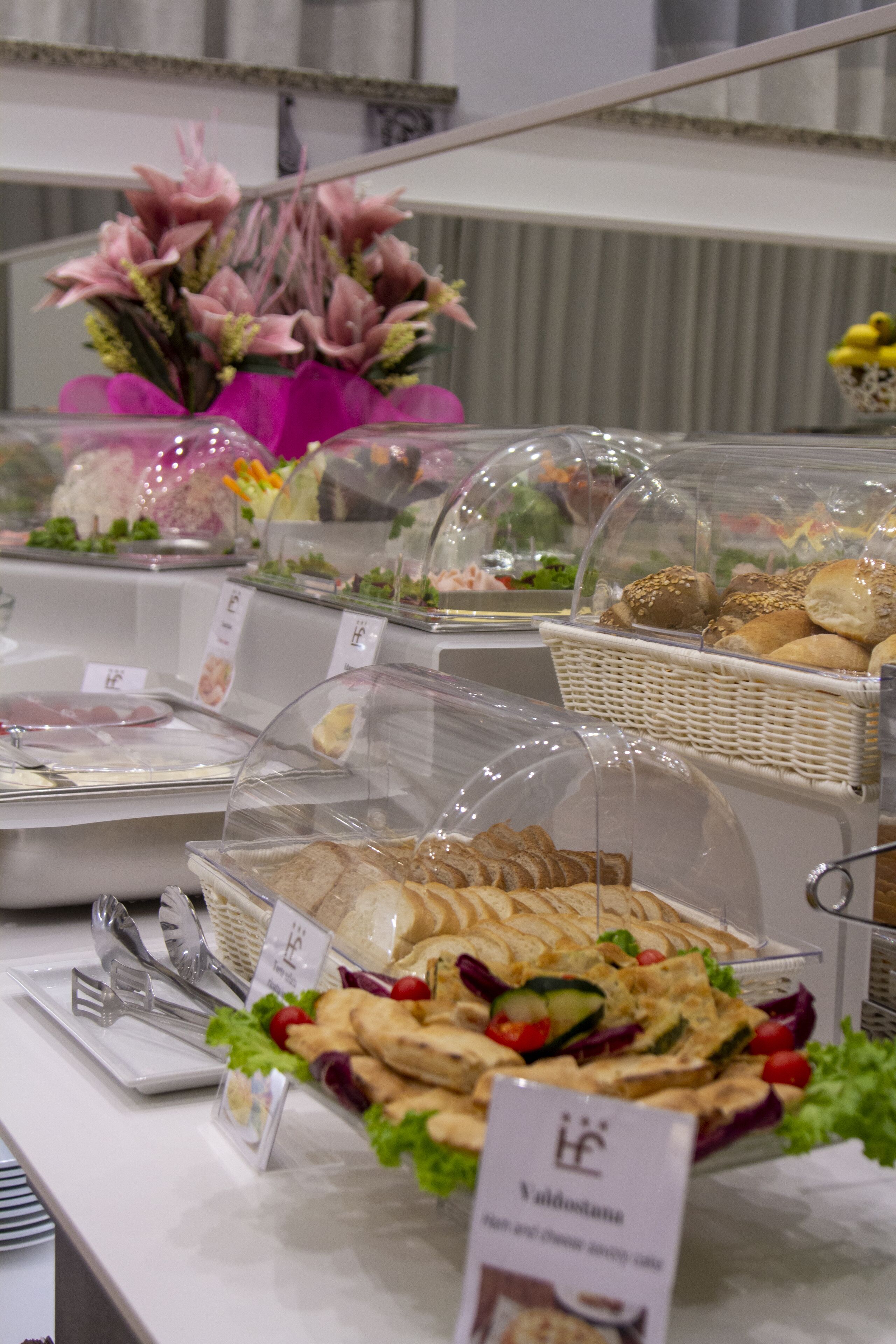 Buffet amb diversos aliments, com ara sandvitxos, amanides i pa, presentats en recipients transparents.