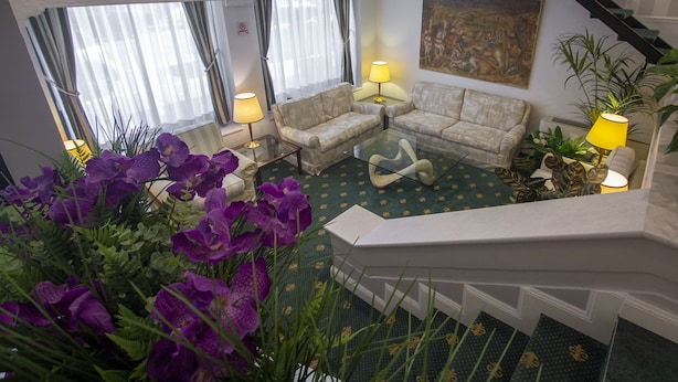 Un hall d’hôtel avec un canapé, des fauteuils, une table basse en verre et un escalier.