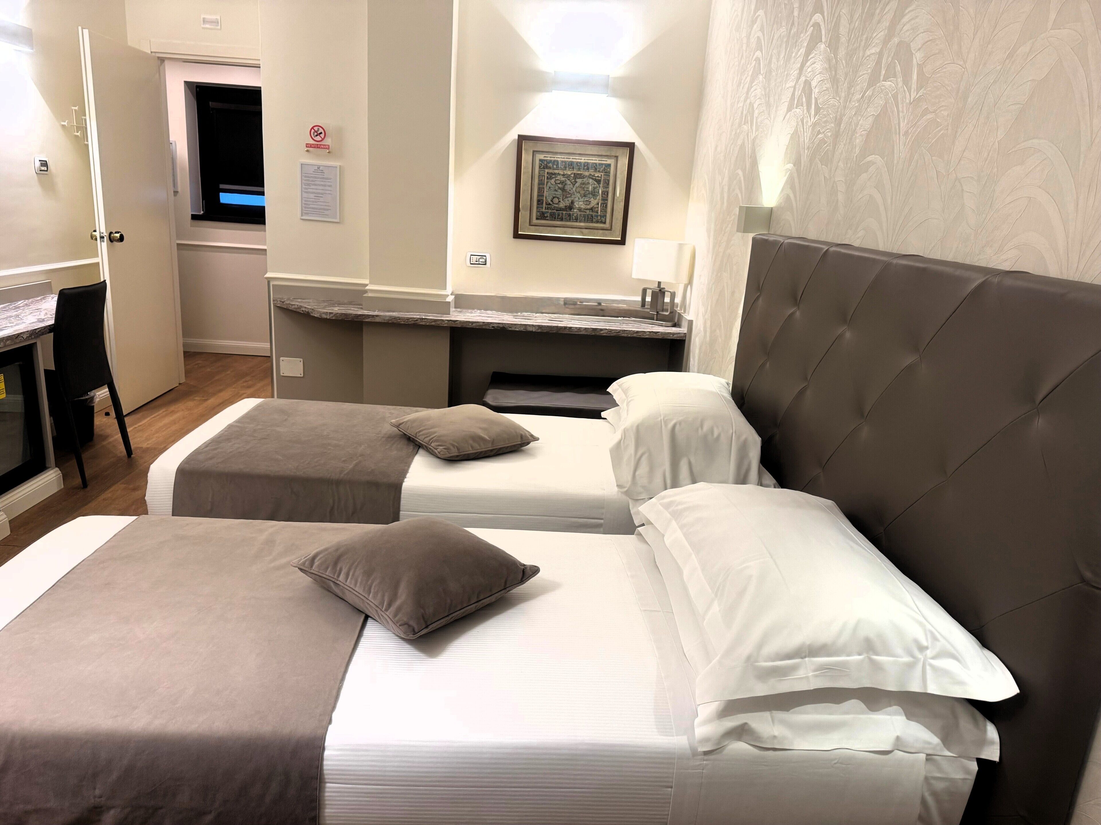 A hotel room with two beds, a desk, and a kitchenette.