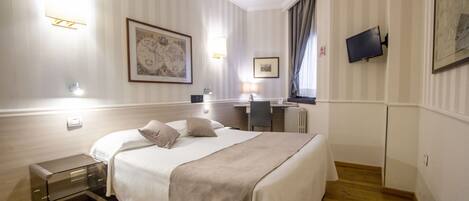 Una habitación de hotel con cama, mesita de noche, lámpara y escritorio con silla.