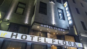 La façade d’un hôtel de nuit, avec une enseigne lumineuse indiquant « HÔTEL FLORA ».