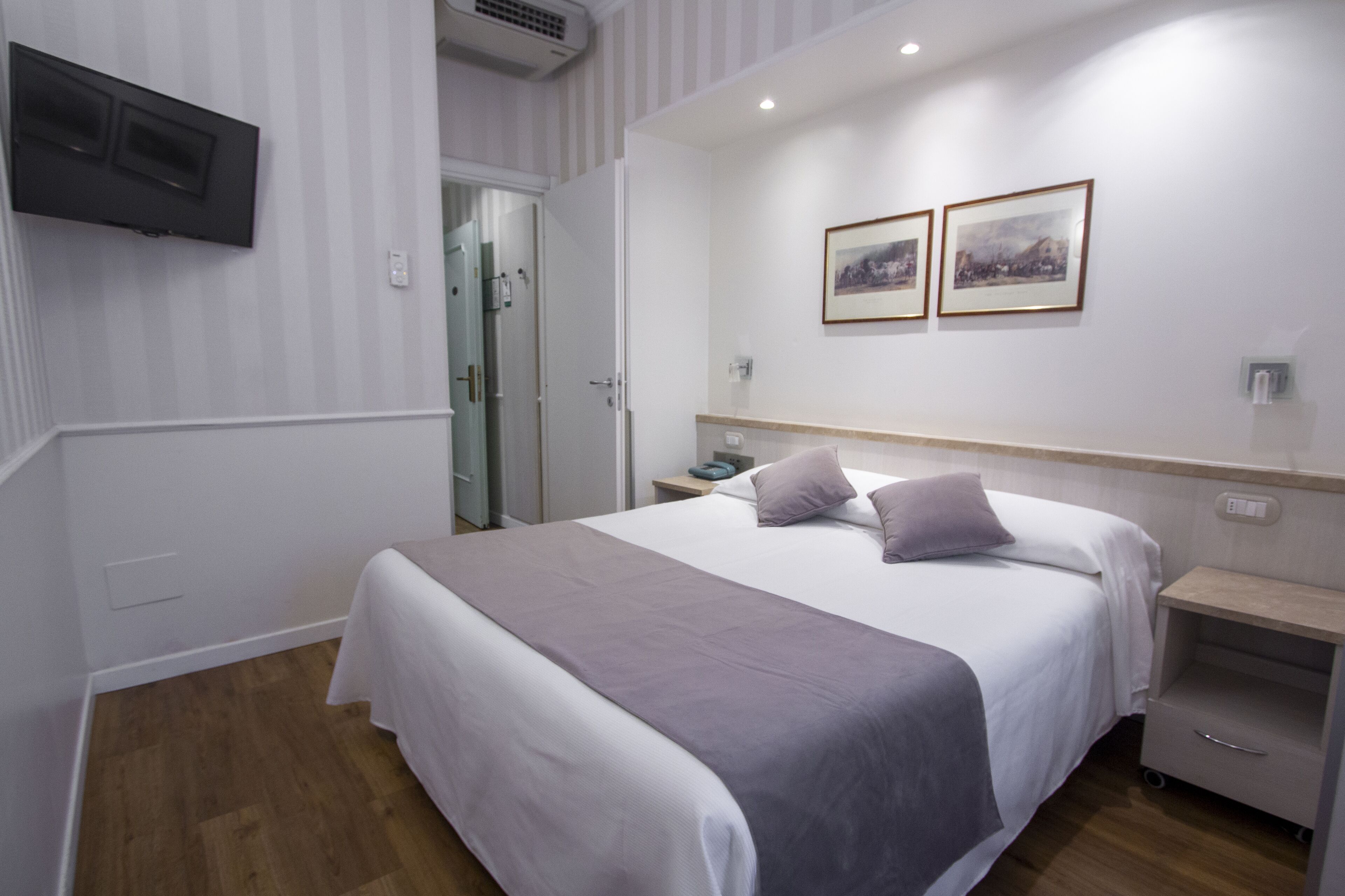 Une chambre d’hôtel bien rangée, avec un lit, une table de chevet et un téléviseur fixé au mur.