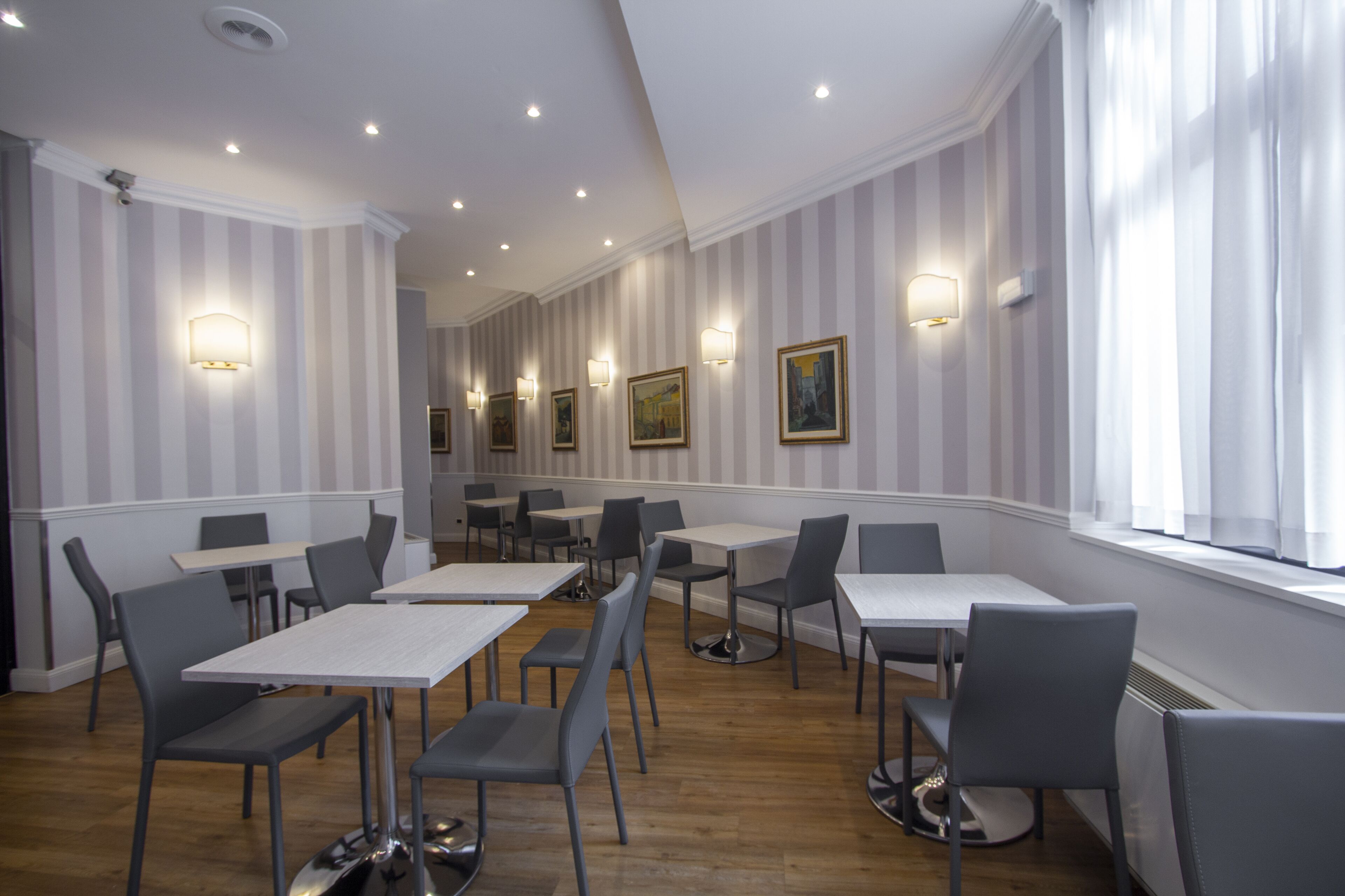 A dining area with striped wallpaper, tables, chairs, and wall-mounted lights.